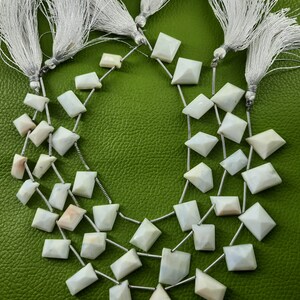 May include: A strand of white opal gemstone beads with a faceted, square shape. The beads are strung on silver wire and are separated by small silver spacers. The beads are arranged in a loose, flowing pattern.