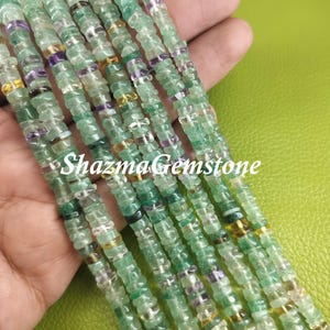 May include: A strand of green, clear, and purple gemstone beads. The beads are faceted and have a slightly irregular shape. The beads are strung on a clear thread. The strand is approximately 18 inches long. Shazma Gemstone is printed on the image.