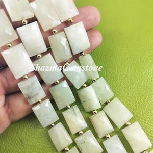 May include: A strand of white rectangular gemstone beads with gold spacers. The beads are faceted and have a translucent appearance. "ShazmaGemstone" is written on the image.