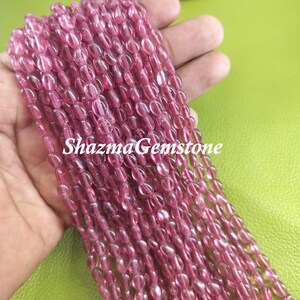 Puede incluir: Una hebra de cuentas de piedras preciosas ovaladas de color rosa. Las cuentas son translúcidas y tienen un ligero brillo. Las cuentas están enhebradas en un hilo transparente.