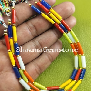 May include: A strand of colorful glass beads, featuring alternating colors of red, yellow, blue, white, and green. The beads are cylindrical in shape and have a glossy finish. The beads are strung on a gold thread.