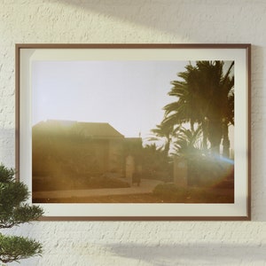 Op de afbeelding: Een ingelijste foto van een gebouw met palmbomen op de voorgrond. De foto is genomen bij zonsondergang en heeft een warme, gouden tint.