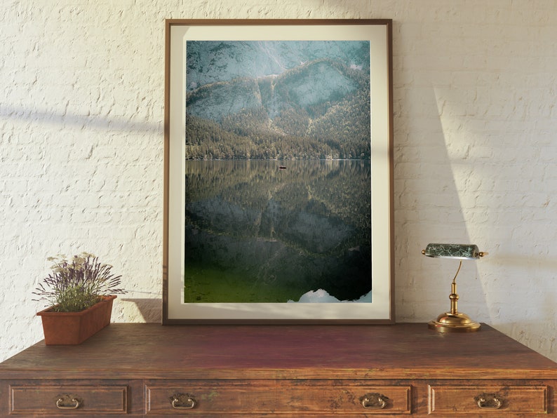 May include: A framed photograph of a mountain lake with a reflection of the surrounding trees and mountains. The water is a deep green color and the sky is a light blue.