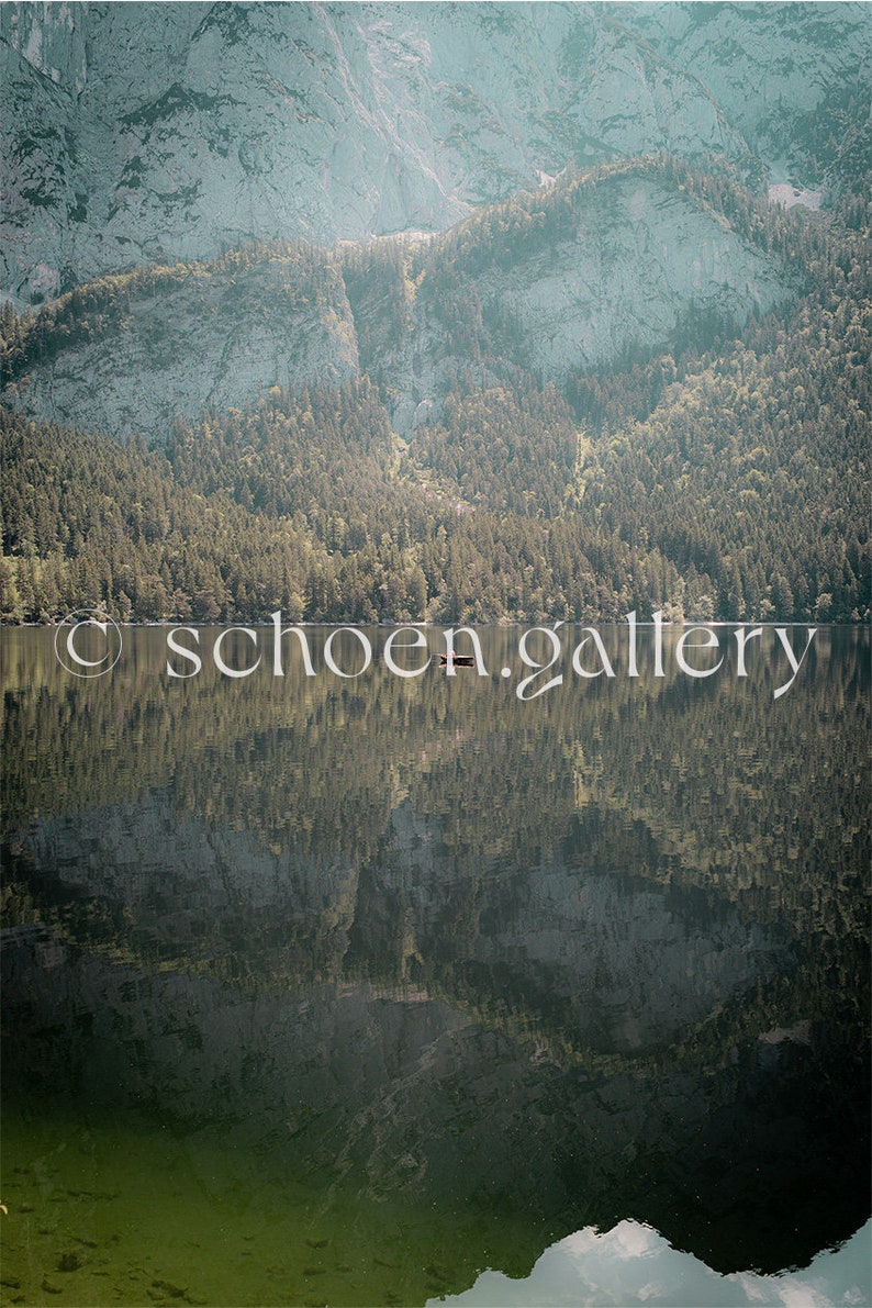 May include: A serene mountain lake with a reflection of the surrounding forest and mountains. The water is calm and still, creating a mirror-like surface.