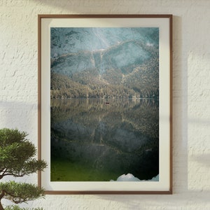May include: A framed photograph of a mountain lake with a small boat in the distance. The water is calm and reflects the mountains and trees surrounding the lake.