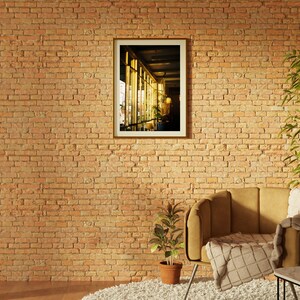 Puede incluir: Un sill&oacute;n marr&oacute;n con una manta de tiro blanca y marr&oacute;n se encuentra frente a una pared de ladrillo. Un cuadro enmarcado de una ventana con luz que entra por ella cuelga de la pared. Una peque&ntilde;a planta en maceta se encuentra en el suelo frente al sill&oacute;n.