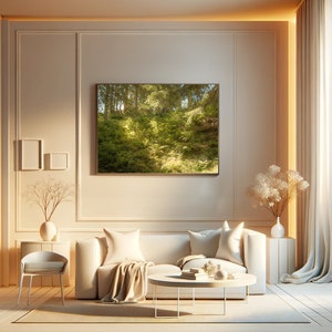 May include: A white sofa with two pillows and a throw blanket sits in a living room with a white coffee table and a framed print of a green forest scene on the wall.