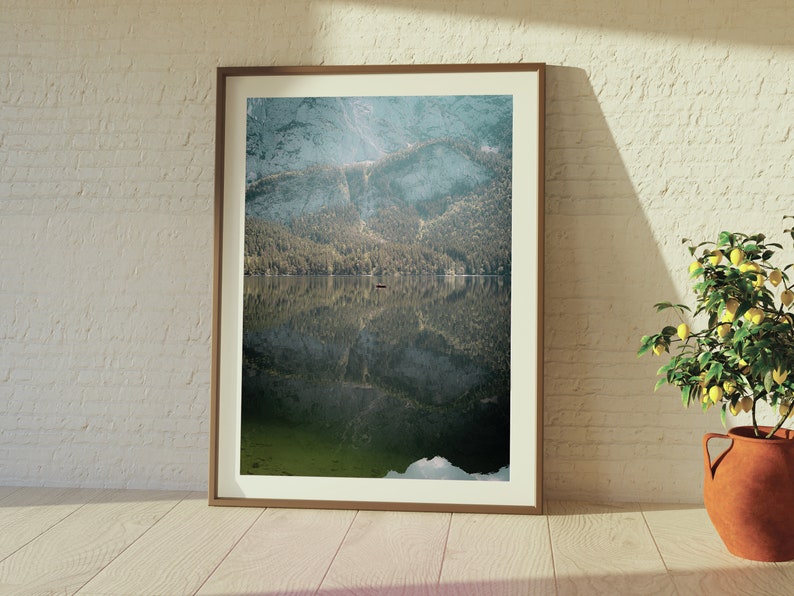 May include: A framed photograph of a mountain lake with a small boat in the middle of the lake. The mountains are reflected in the water. The photo is hanging on a white brick wall.