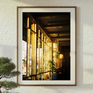 Puede incluir: Una fotograf&iacute;a enmarcada de una habitaci&oacute;n con grandes ventanales, mostrando una vista de una ciudad. Las ventanas est&aacute;n hechas de paneles de vidrio con marcos de madera. La luz del sol entra por las ventanas, iluminando la habitaci&oacute;n. Una planta en maceta se encuentra en el alf&eacute;izar de la ventana, agregando un toque de vegetaci&oacute;n al espacio.