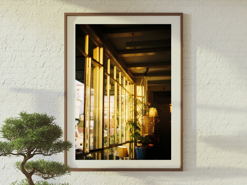 Puede incluir: Una fotograf&iacute;a enmarcada de una habitaci&oacute;n con grandes ventanales, mostrando una vista de una ciudad. Las ventanas est&aacute;n hechas de paneles de vidrio con marcos de madera. La luz del sol entra por las ventanas, iluminando la habitaci&oacute;n. Una planta en maceta se encuentra en el alf&eacute;izar de la ventana, agregando un toque de vegetaci&oacute;n al espacio.