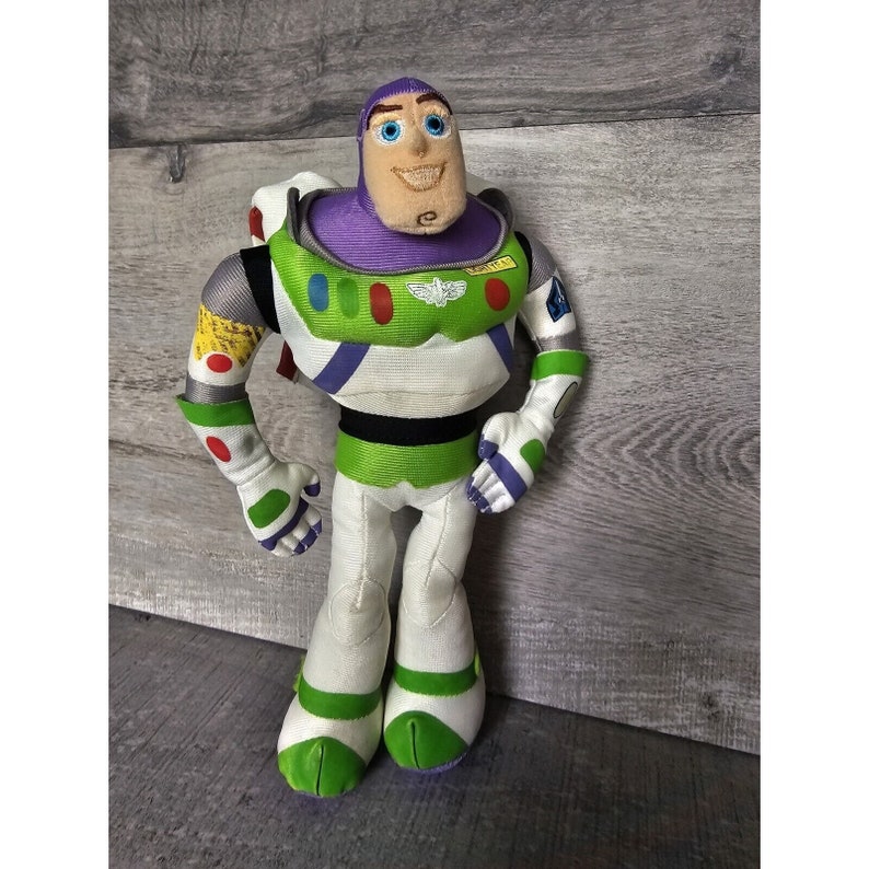 Peut inclure: Un jouet en peluche de Buzz l'&Eacute;clair de la franchise Toy Story. Le jouet porte sa combinaison de ranger spatial signature avec une plaque de poitrine violette, des jambes vertes et blanches et un casque vert et blanc. Le jouet a un visage amical avec des yeux bleus et un sourire.