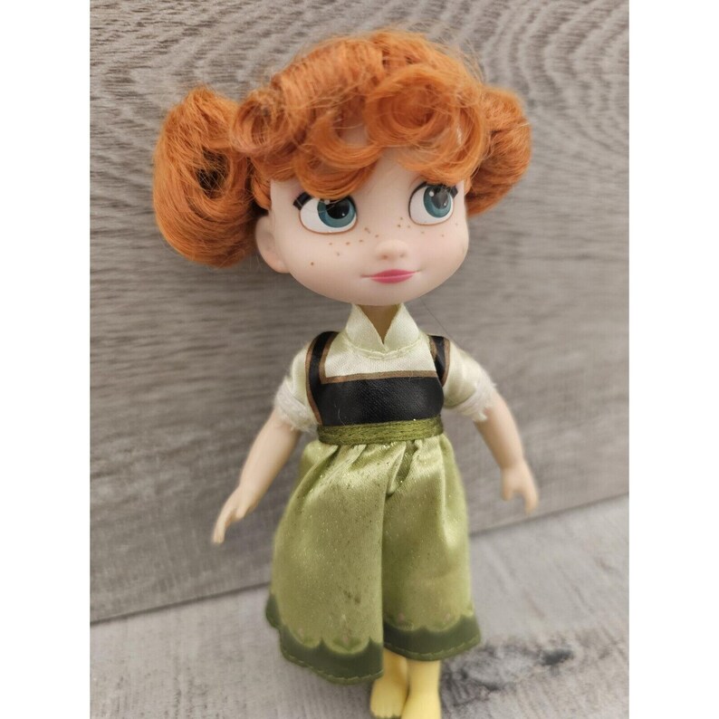 Puede incluir: Una peque&ntilde;a mu&ntilde;eca con el pelo rojo rizado, que lleva un vestido verde con un chaleco negro y un cuello blanco. La mu&ntilde;eca tiene ojos azules y pecas.