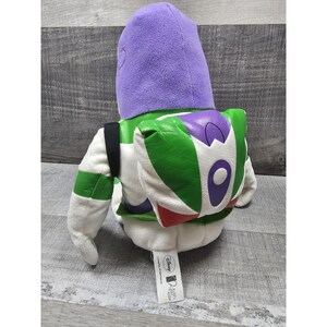 May include: A soft Buzz Lightyear toy from the Disney Pixar Toy Story franchise. The toy has a purple helmet, green and white spacesuit, and a jetpack. The toy is designed for children.