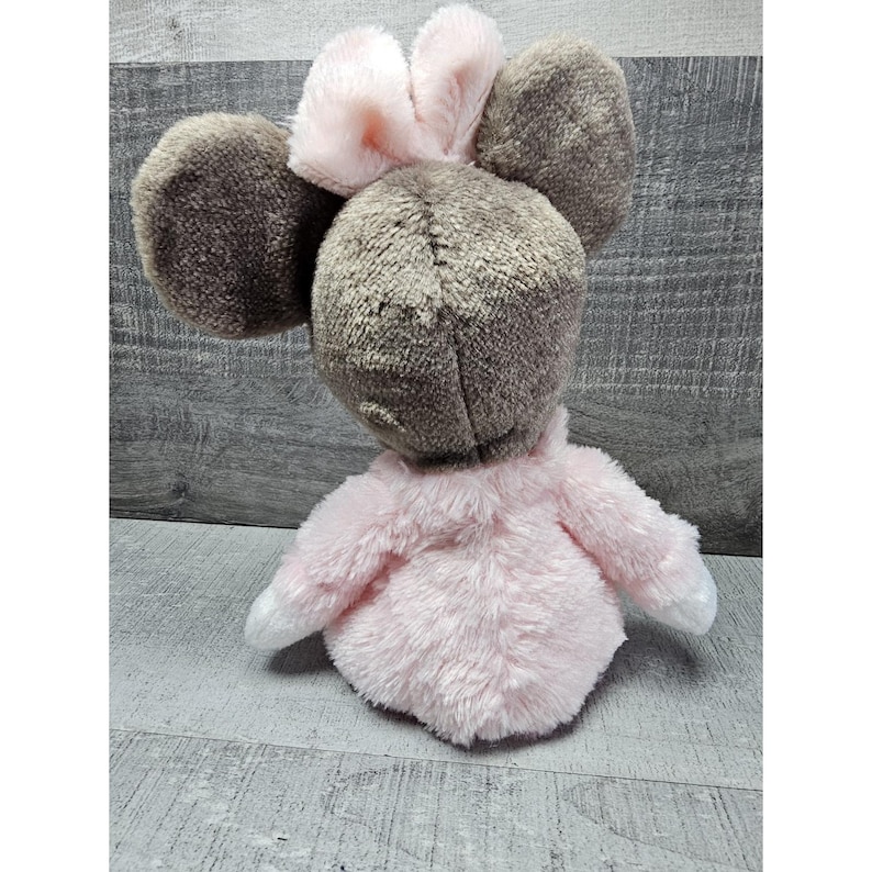 May include: A plush toy mouse with large, round ears and a pink bow. The mouse is primarily gray and pink, with white accents on the paws. The toy has a soft, fuzzy texture and is designed to resemble a cartoon character.