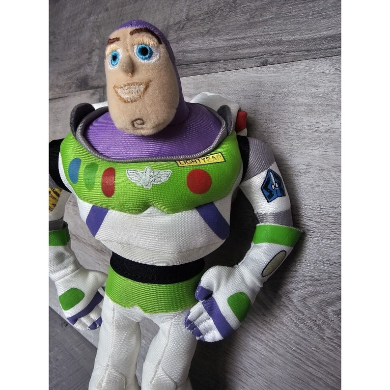 Peut inclure: Un jouet en peluche de Buzz l'&Eacute;clair de la franchise Toy Story. Le jouet porte sa combinaison de ranger spatial signature avec un gilet violet, une chemise &agrave; rayures vertes et blanches et un casque blanc. Le jouet a un visage amical avec des yeux bleus et un l&eacute;ger sourire. La poitrine du jouet a un patch qui indique "LIGHTYEAR".