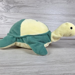 Pode incluir: Um brinquedo de pelúcia em forma de tartaruga com uma textura macia e aveludada. O casco é de um verde floresta profundo com um painel central amarelo pálido. A cabeça, o pescoço e a parte inferior também são de cor amarelo pálido.