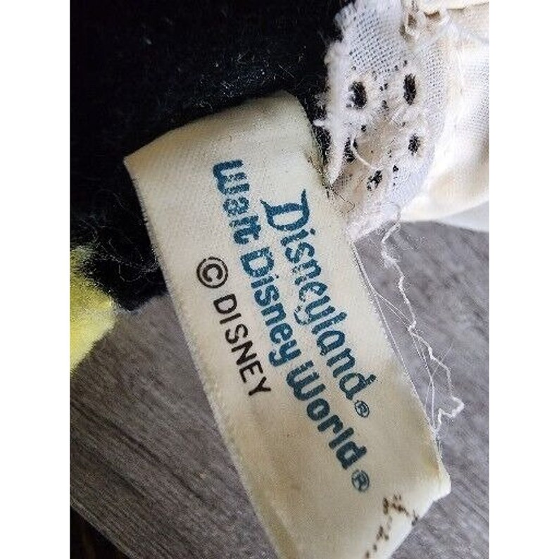 Peut inclure: &Eacute;tiquette blanche avec le texte "Disneyland&reg; Walt Disney World&reg; &copy; DISNEY" sur un jouet en peluche noir et blanc.