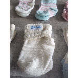 Puede incluir: Un par de calcetines blancos para beb&eacute; con un pu&ntilde;o de punto blanco y una etiqueta azul que dice "Carter's&reg;".