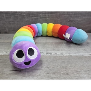 May include: A plush, rainbow-colored caterpillar toy with a smiling purple head. The caterpillar's body is segmented in a spectrum of colors, including red, orange, yellow, green, blue, and purple. The toy is designed for children.