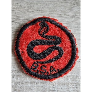 May include: A red and black embroidered patch with a snake design and the letters "BSA" in the bottom circle.