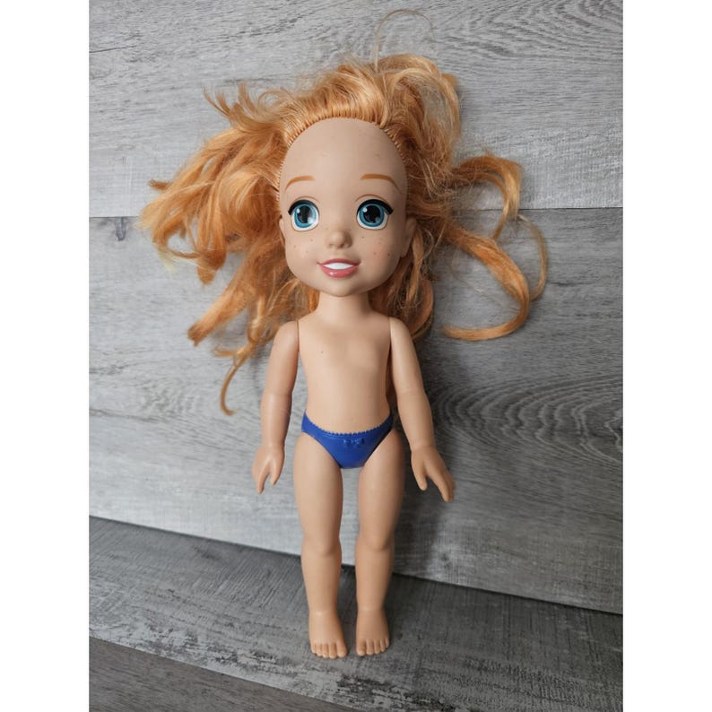 May include: A red-haired doll with blue eyes and a blue swimsuit. The doll is made of plastic and has a realistic face.