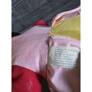 May include: Close-up of a plush toy with pink, red, and yellow fabric. The pink fabric has white polka dots. A tag reads "Mattel, Inc. Hawthorne, CA 90250 U.S.A. MADE IN CHINA Manufactured for Mattel".