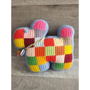 May include: A colorful crocheted dog toy with a patchwork design in shades of red, orange, yellow, green, blue, purple, and pink. The toy has a blue body and a long, thin tail.