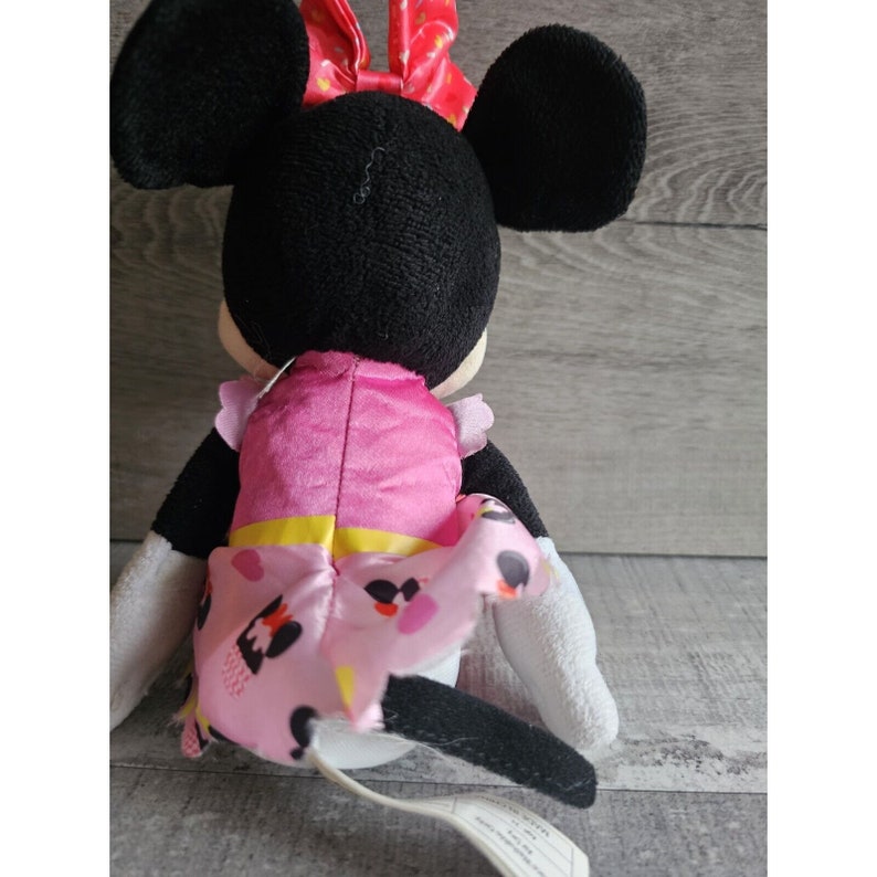 May include: A plush Minnie Mouse toy wearing a pink dress with a yellow sash and white polka dots. She has a red bow with white polka dots on her head.