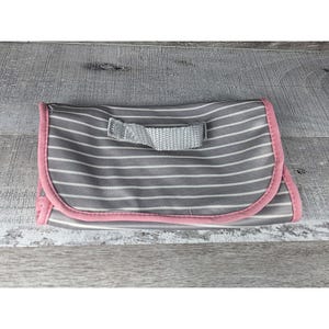 May include: A folded changing mat with grey and white stripes, a pink trim, and a grey handle. The mat is designed for portability and features a simple, clean design.