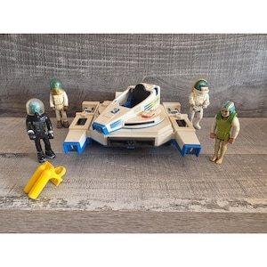 May include: A white ceramic mug with a black handle and the text "But First, Coffee" in a bold, black font. The mug is set against a blurred background, suggesting a cozy setting.