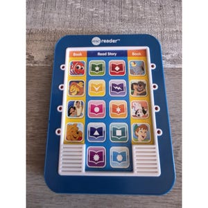 Op de afbeelding: Blauw elektronisch "me reader" boek met kleurrijke illustraties van Disney-personages. Voorzien van knoppen met de tekst "Book" en "Read Story". Bevat afbeeldingen van personages als Simba, Winnie de Poeh en Assepoester.