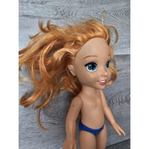 May include: A doll with red hair, blue eyes and freckles. The doll is wearing a blue swimsuit.