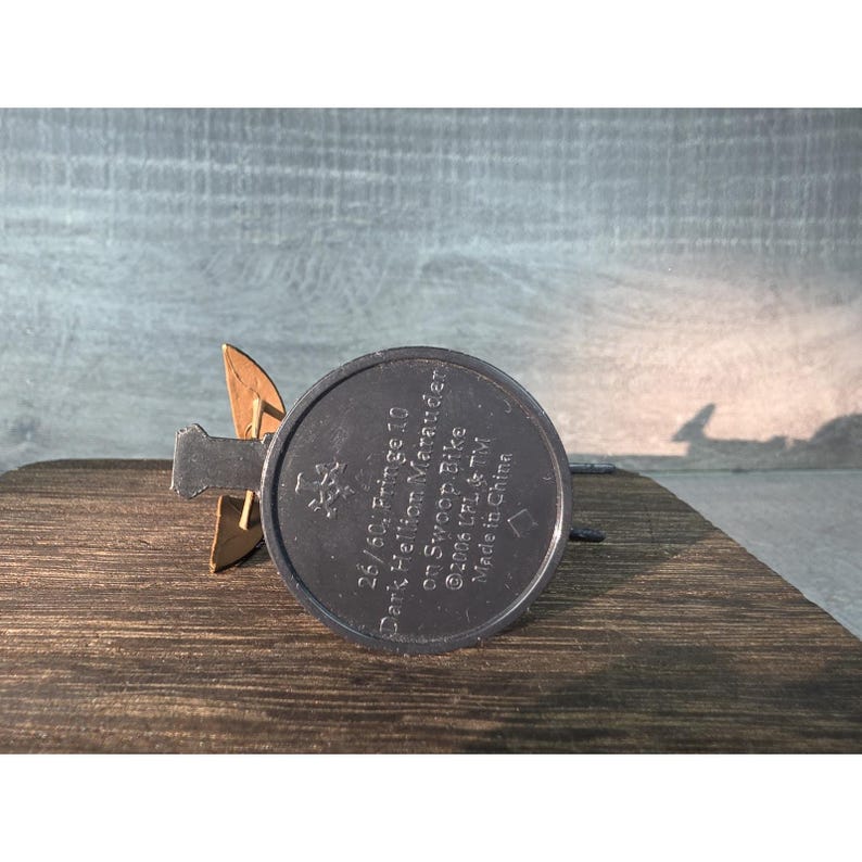 May include: A black and gold toy vehicle, the Dark Hellion Marauder on a Swoop Bike, is displayed on a wooden surface. The text on the base reads "26/60: Fringe 10" and "&copy;2006 UFL & TM Made in China."