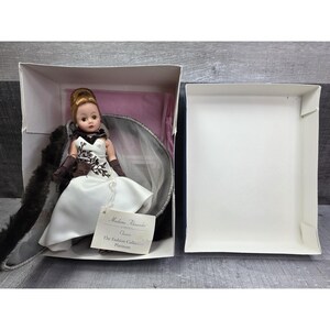 May include: A Madame Alexander doll from The Fashion Collection Platinum series. The doll is in a white dress with black embroidery and brown gloves. It is in its original box with a fur stole and a tag that reads "Madame Alexander".