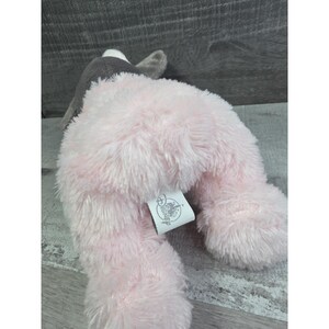 Puede incluir: Un peluche rosa con forma de animal con orejas grises y cabeza gris. El juguete tiene una textura esponjosa y una etiqueta adherida a su cuerpo.