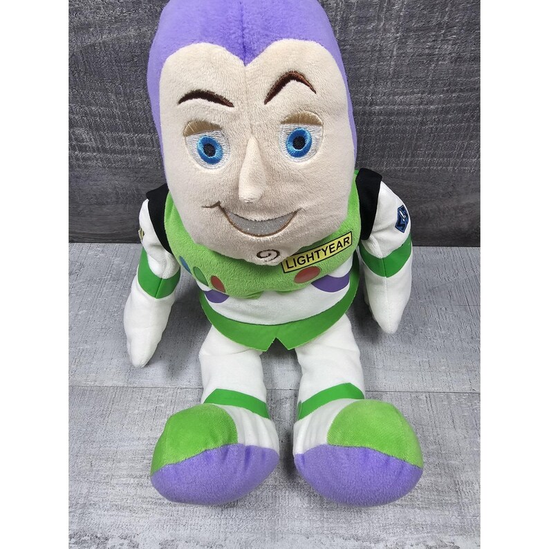 May include: A soft toy of Buzz Lightyear from the Toy Story films. The doll has a purple head, a white face with blue eyes, and a green and white spacesuit. The word "LIGHTYEAR" is printed on the chest.