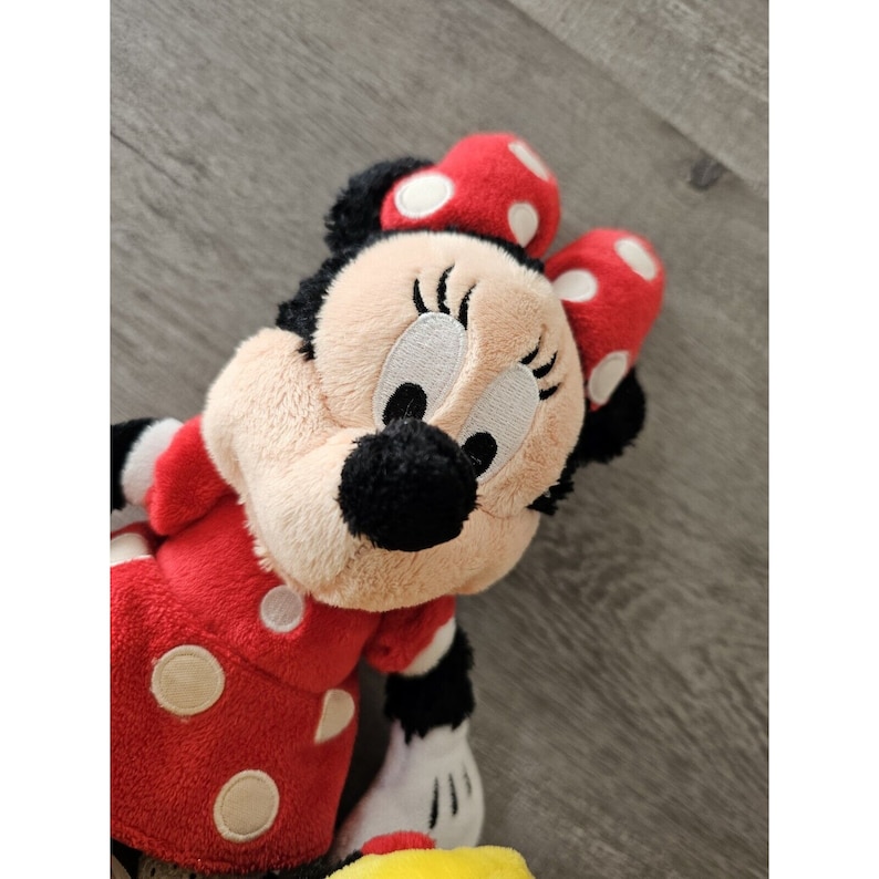 K&ouml;nnte beinhalten: Ein Pl&uuml;schtier von Minnie Mouse, die ein rotes Kleid mit wei&szlig;en Punkten und eine rote Schleife mit wei&szlig;en Punkten tr&auml;gt. Ihre Augen sind geschlossen und sie hat ein breites L&auml;cheln.