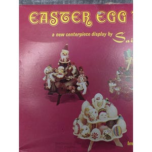 May include: A magenta product box featuring the text EASTER EGG, a new centerpiece display by Sai. The box displays two tiered stands: one holding small figurines and another holding multiple decorated eggs with various patterns and colors.