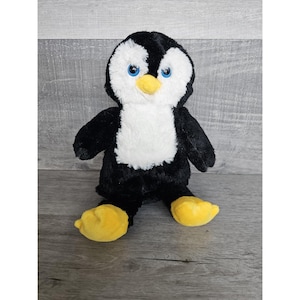 May include: A black and white plush penguin with yellow feet. The penguin has blue eyes and a yellow beak.