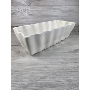 May include: A rectangular white ceramic planter with a wavy, scalloped edge design. The vessel features a glossy finish with subtle vertical ridges along the exterior walls, creating a textured appearance throughout the entire structure.