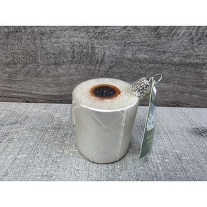 Puede incluir: Un adorno navideño novedoso con forma de rollo de papel higiénico. El adorno es blanco con un patrón de diamantes y un centro marrón. Tiene una tapa plateada y una cuerda plateada para colgar.