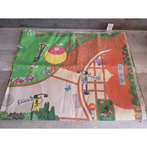 Könnte beinhalten: Eine farbenfrohe Spielmatte mit einer skurrilen Stadtszene. Die Matte hat eine grüne Rasenfläche, Ziegelstraßen und Gebäude. Der Text auf der Matte lautet "Lollipop Pkwy West" und "Candy Cove Rd West". Die Matte ist für Kinderspiele konzipiert.