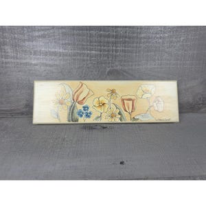May include: A rectangular wooden plaque featuring a hand-painted illustration of various wildflowers in shades of yellow, orange, and blue. The artwork includes detailed line work and soft color washes on a light, natural wood grain background.