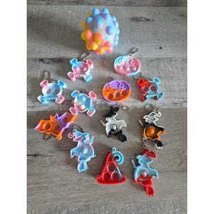 May include: A collection of colorful fidget toys, including skull, bat, witch, and hat shapes, with keychains. A large, textured, multi-colored ball is also present. The toys are in various colors, including blue, pink, orange, and red.