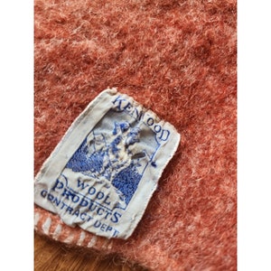 May include: A close-up of a red wool blanket with a white label that reads "Kenwood Wool Products Contract Dept."