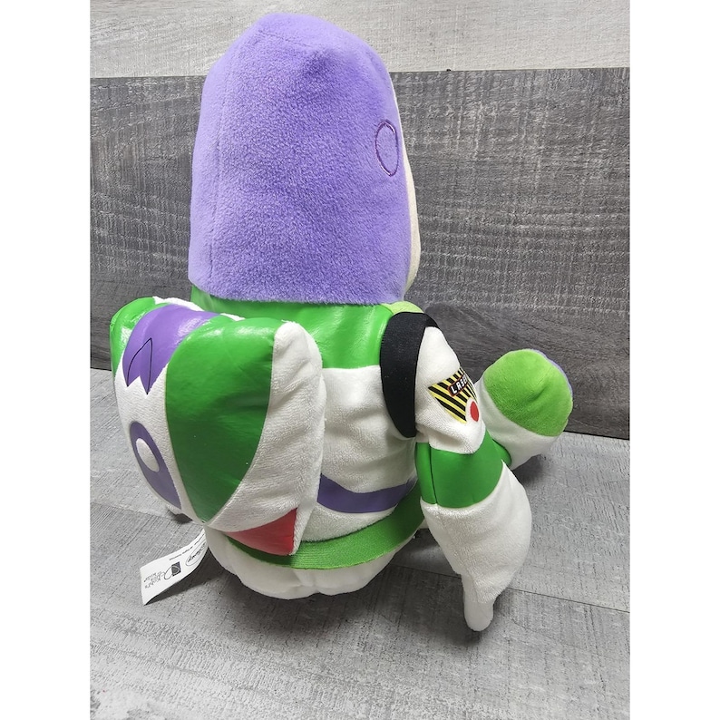 May include: A soft Buzz Lightyear toy, with a purple helmet, green and white spacesuit, and white gloves. The toy has a detailed design with black, red, and purple accents. A collectible item from the Toy Story franchise.