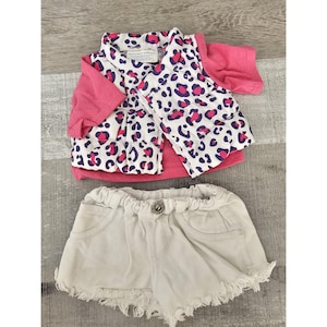 Può includere: Un gilet a stampa leopardata rosa e bianca con una camicia rosa a maniche corte e pantaloncini di jeans bianchi con bordi sfrangiati.