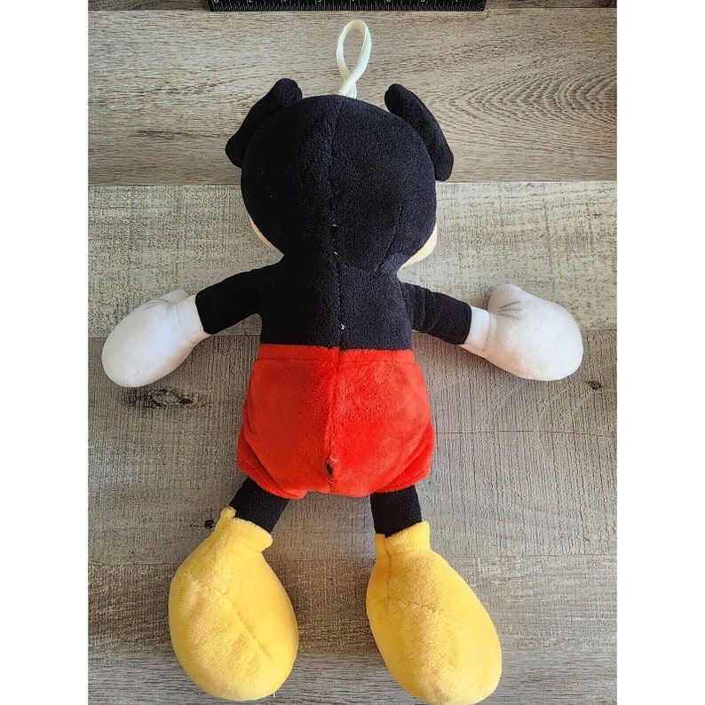 May include: A plush Mickey Mouse toy with black fur, red shorts, and yellow shoes. The toy has a loop on the top of its head.