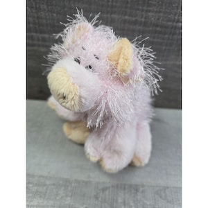 Puede incluir: Un juguete de peluche de cerdo rosa con una melena desgreñada y orejas caídas. El cerdo tiene un cuerpo rosa claro, un hocico beige y ojos negros pequeños. El juguete está hecho de material suave y difuso.