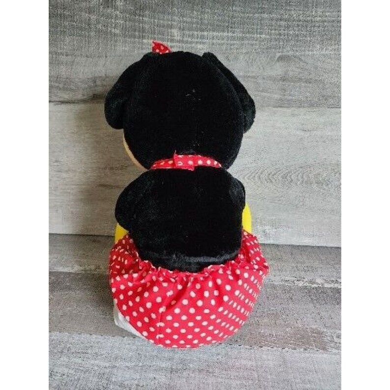 Pu&ograve; includere: Un giocattolo di peluche nero con una gonna a pois rossi e bianchi. Il giocattolo ha un fiocco nero intorno al collo e un fiocco rosso sulla testa.